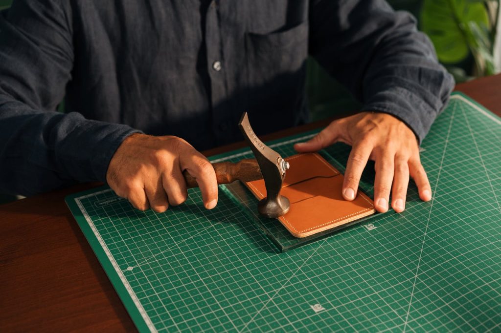 Artisan precisely crafting leather product with hand tools on cutting mat.