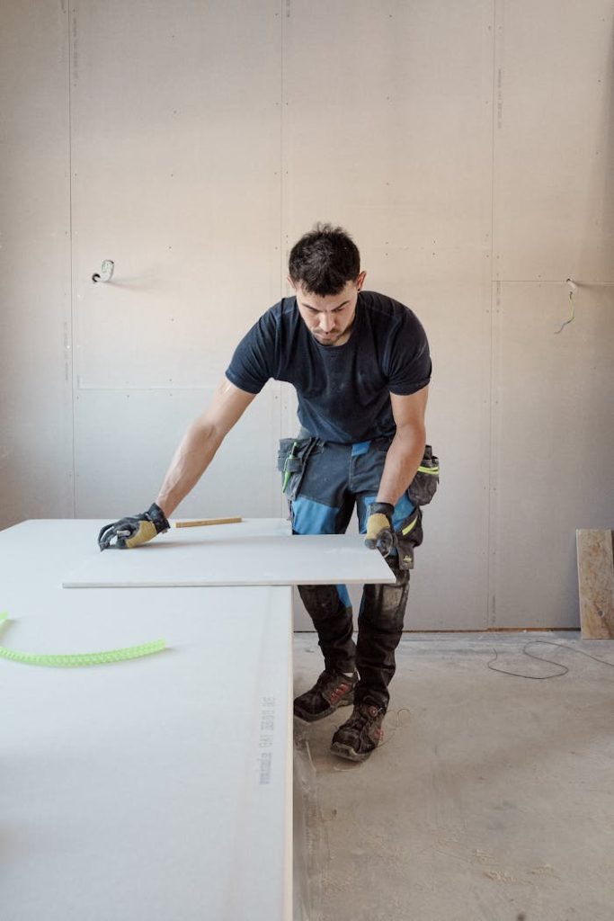A blue collar worker measuring a plank indoors in a bright workshop.